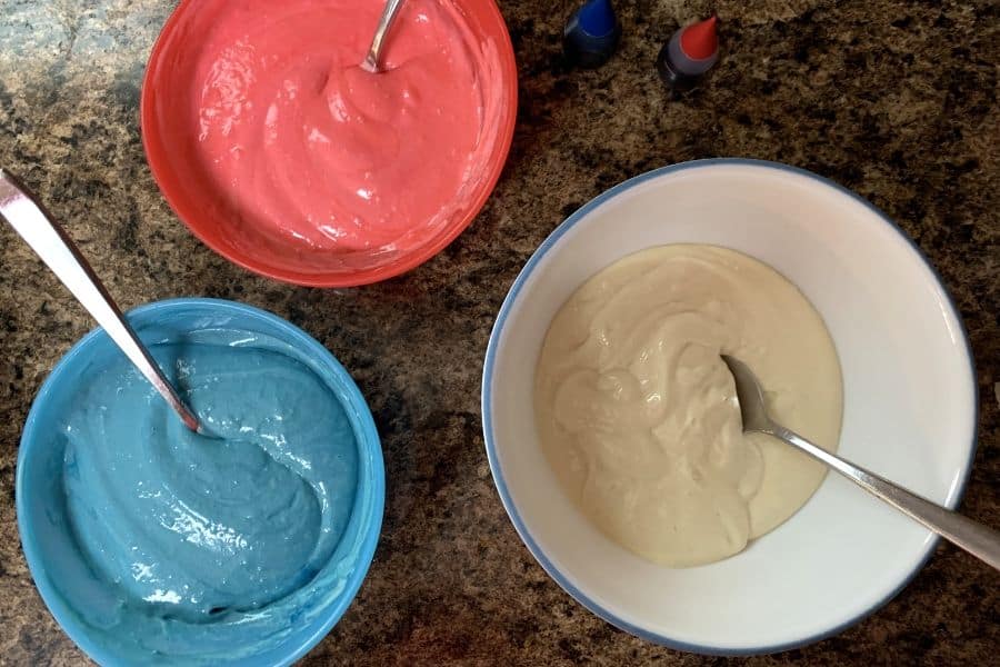 three bowls of cake batter, including blue, red, and white colors.