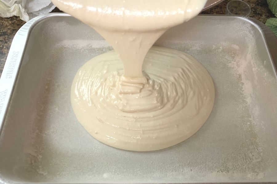 white cake batter being poured into a greased and floured pan