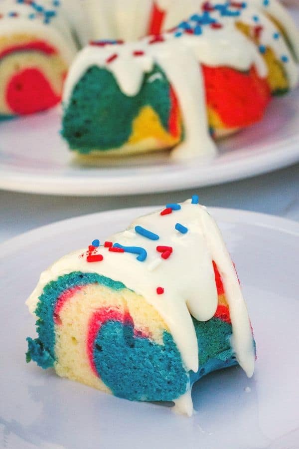 a slice of red, white, and blue bundt cake on a white plate, topped with icing and sprinkles