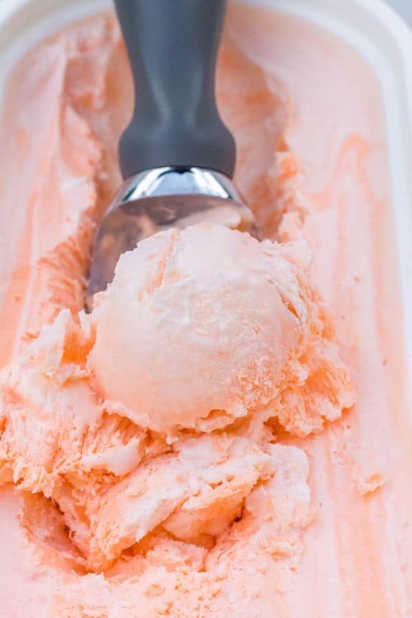 an ice cream scoop while scooping out a serving of orange creamsicle ice cream