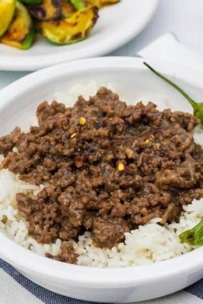 white bowl filled with Instant Pot Korean beef served over white rice, with two shishito peppers in the bowl