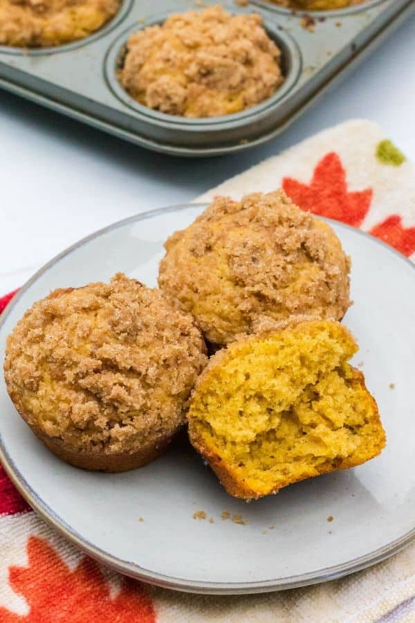 three pumpkin and banana muffins on a plate, with one muffin torn in half