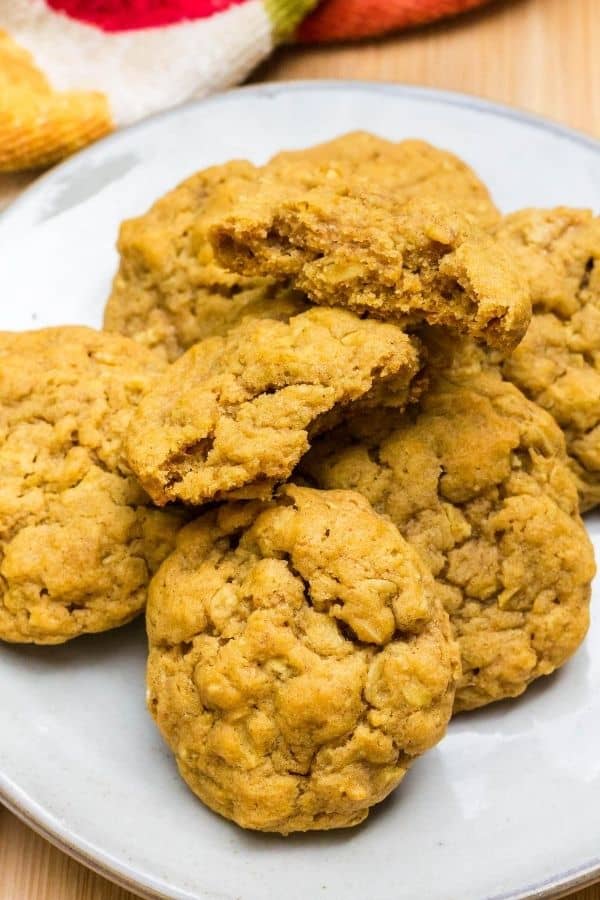 several soft and chewy pumpkin oatmeal cookies on a white plate, with one cookie torn in half