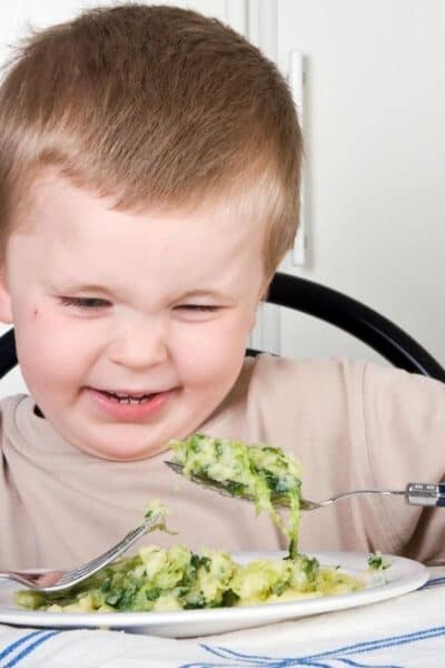 young boy grimacing at a plate of broccoli