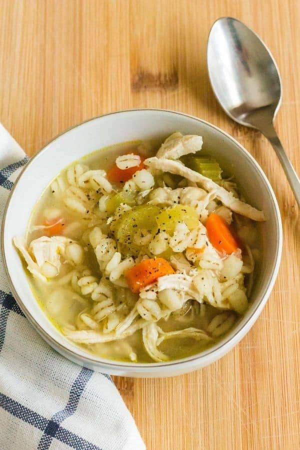 white bowl of Instant Pot chicken barley soup on a cutting board