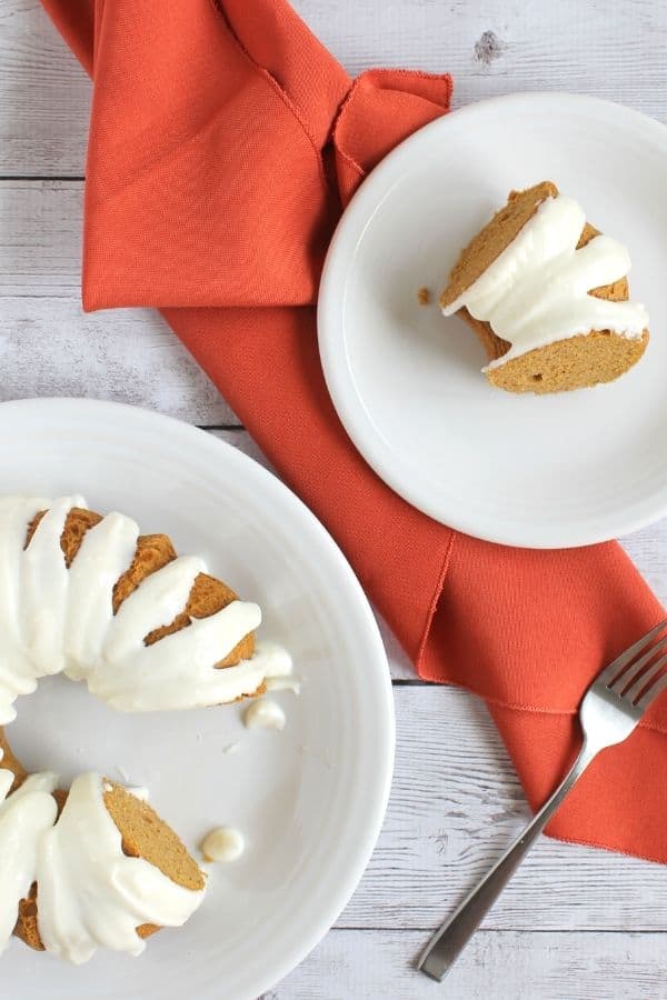 A slice of Instant Pot pumpkin cake on a white dessert plate, next to the entire cake on a serving platter