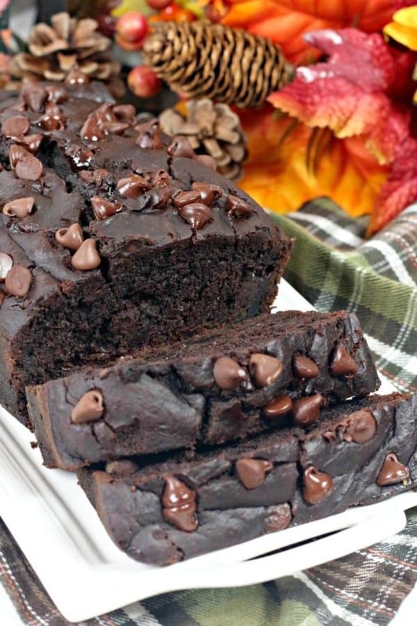 loaf of chocolate pumpkin bread on a white plate, topped with melted chocolate chips, next to fall decor