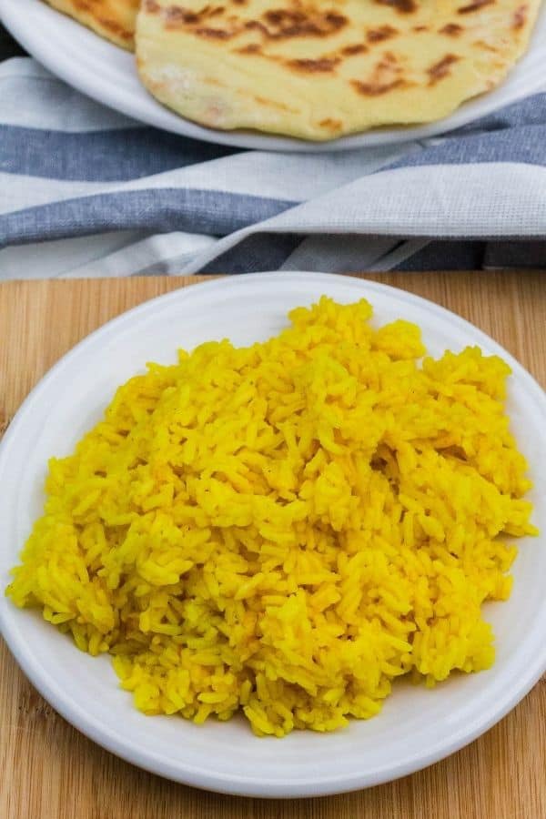 Instant Pot saffron yellow rice on a white plate, next to a plate of homemade naan bread