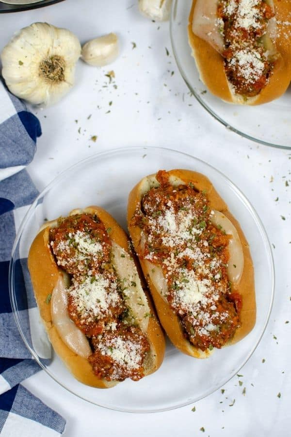 aerial view of two Italian meatball subs on a clear glass plate, next to a blue and white checkered napkin, with the Instant Pot in the background