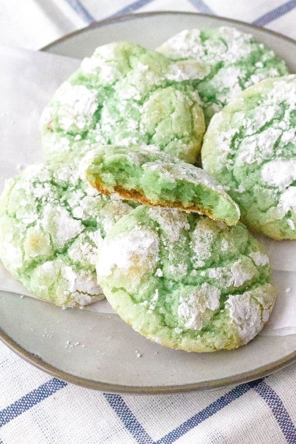 pistachio crinkle cookies on a plate, with one cookie that has a bite taken out of it
