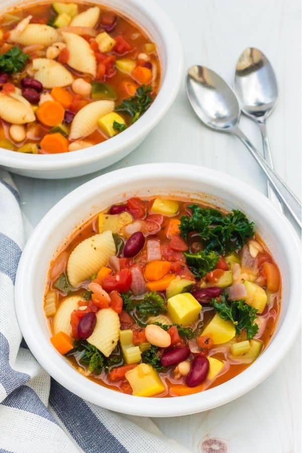 Instant Pot minestrone soup in two white bowls, with two spoons lying next to them on the right and a blue and white kitchen towel on the left.