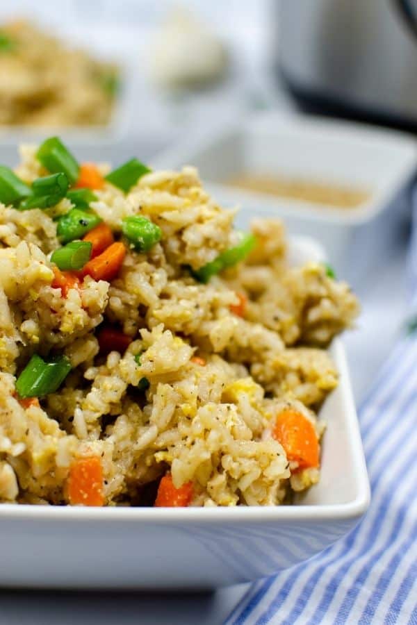 Close-up side view of hibachi style pressure cooker chicken fried rice in a white bowl, next to a blue and white kitchen towel.