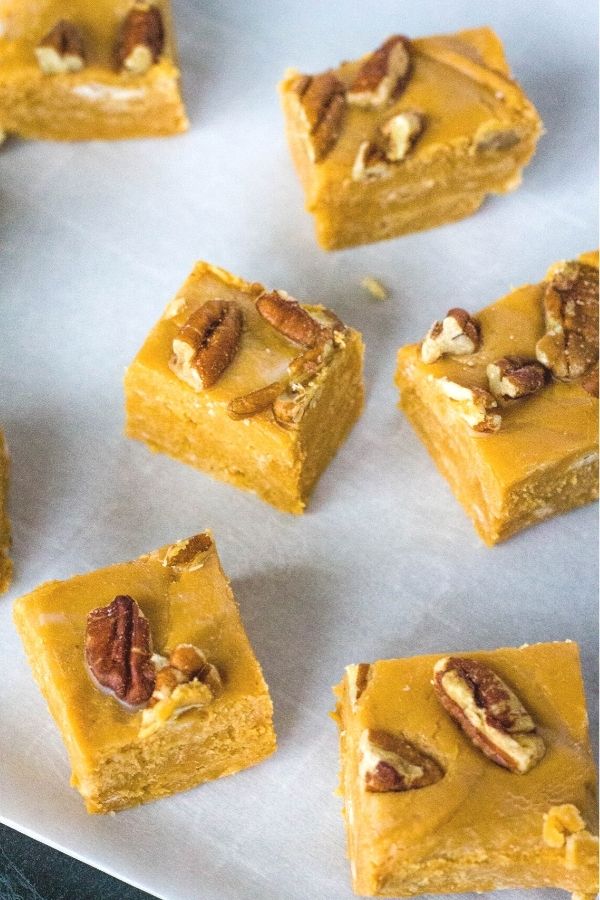 Squares of dulce de leche fudge topped with pecans, spread out on a sheet of parchment paper