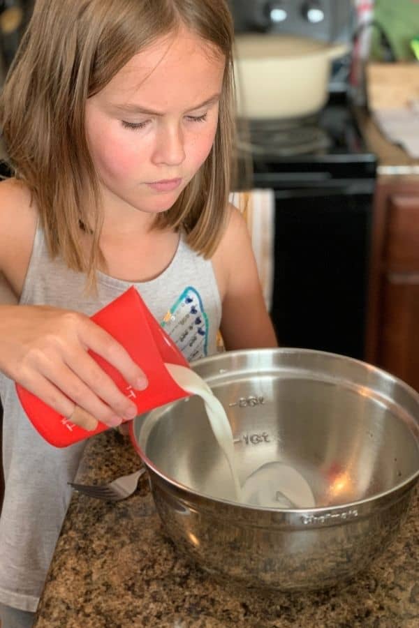 Female child pouring milk into a mixing bowl.