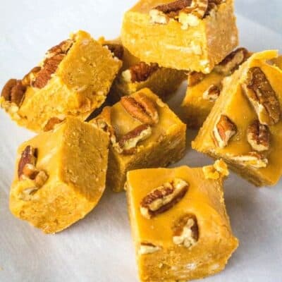 several squares of caramel fudge topped with pecans, stacked on a piece of parchment paper