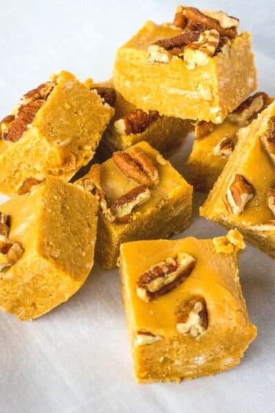 several squares of caramel fudge topped with pecans, stacked on a piece of parchment paper