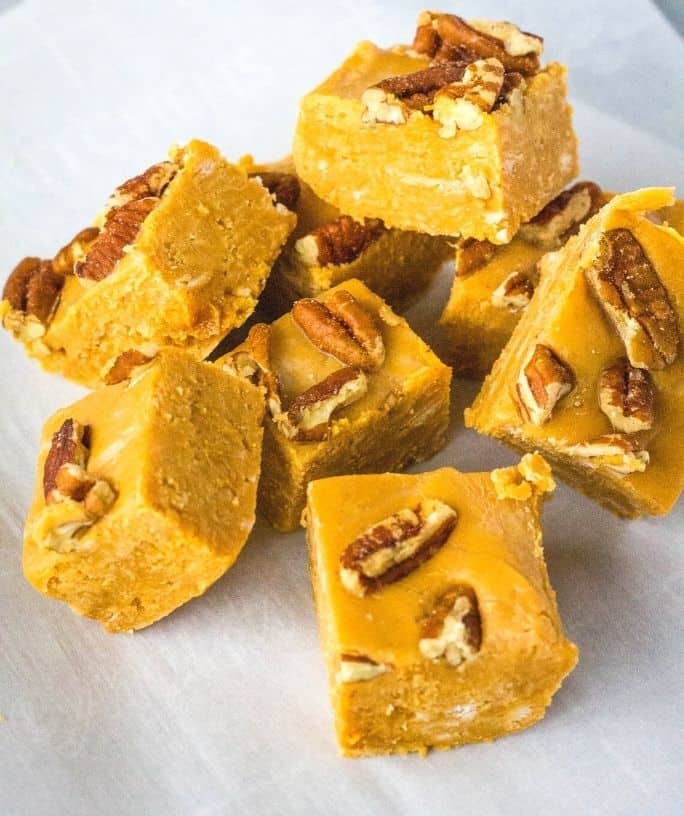 several squares of caramel fudge topped with pecans, stacked on a piece of parchment paper