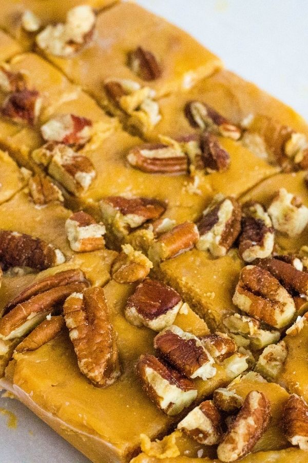 A slab of caramel fudge topped with pecans, freshly cut into squares