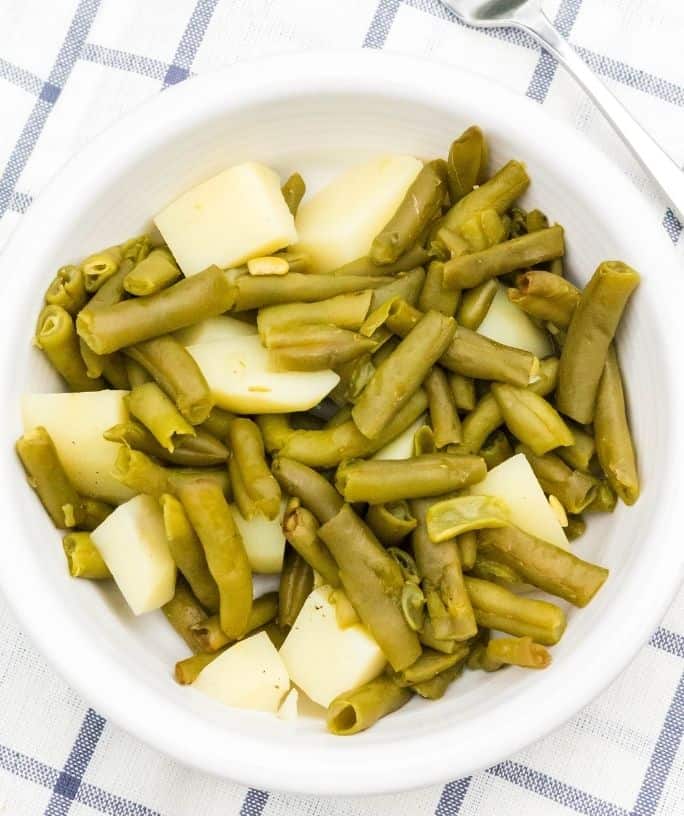 cooked canned green beans and potatoes are in a white bowl on a blue and white cloth, after being cooked in the pressure cooker