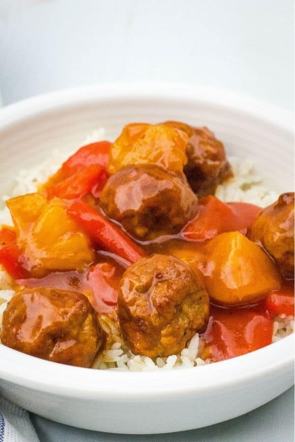 Side view of a white bowl filled with Instant Pot Hawaiian meatballs made with frozen meatballs, plus pineapple, peppers, and tangy sauce.