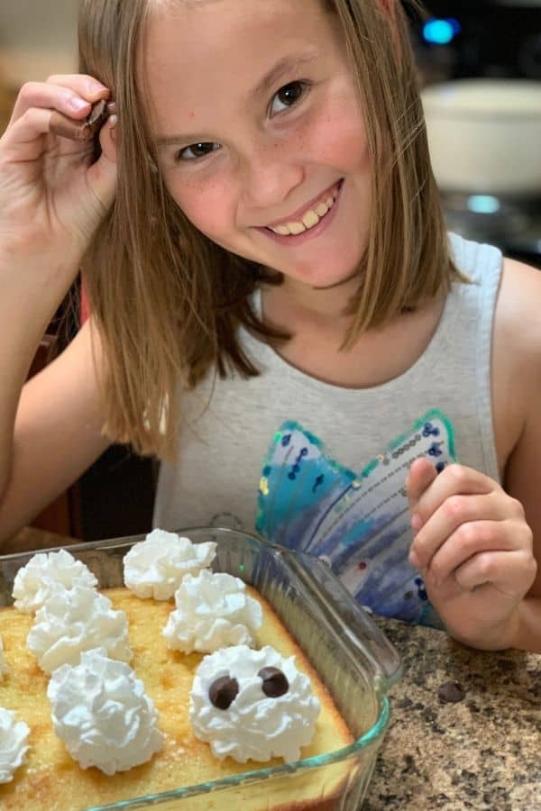 Child smiling while decorating tres leches cakes to look like ghosts.