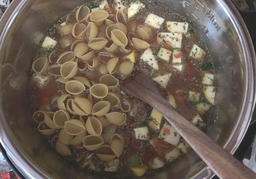 vegetables, pasta, beans, and seasonings mixed in broth in the insert pot for making Instant Pot minestrone soup