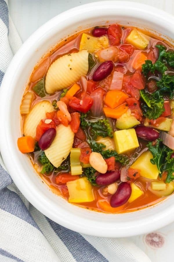 pressure cooker minestrone soup with beans, pasta shells, vegetables, and kale all in a white bowl.