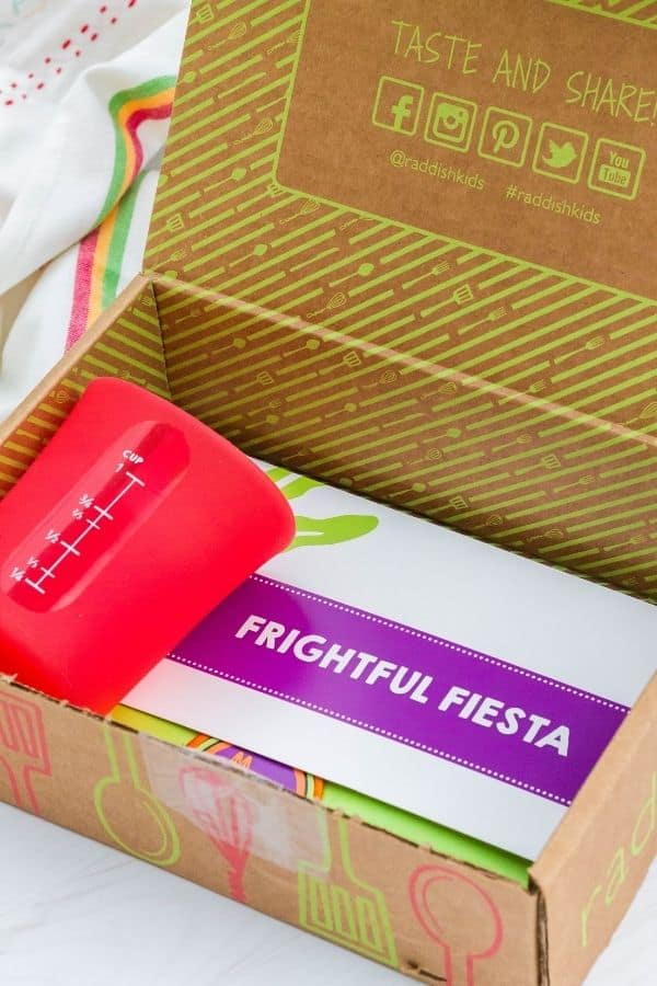 Raddish Kids box containing a red silicone liquid measuring cup as well as a packet titled "Frightful Fiesta."