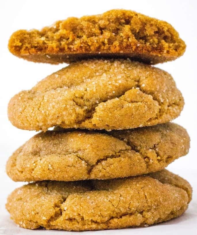 stack of four molasses sugar cookies, with the top cookie broken in half to show the soft inside.