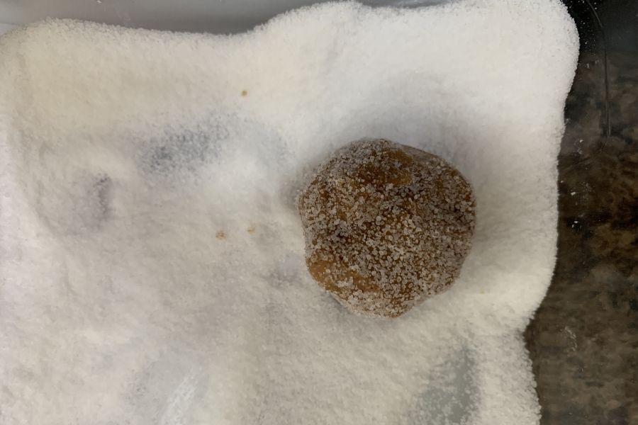 A ball of molasses cookie dough in a dish of sugar for rolling.