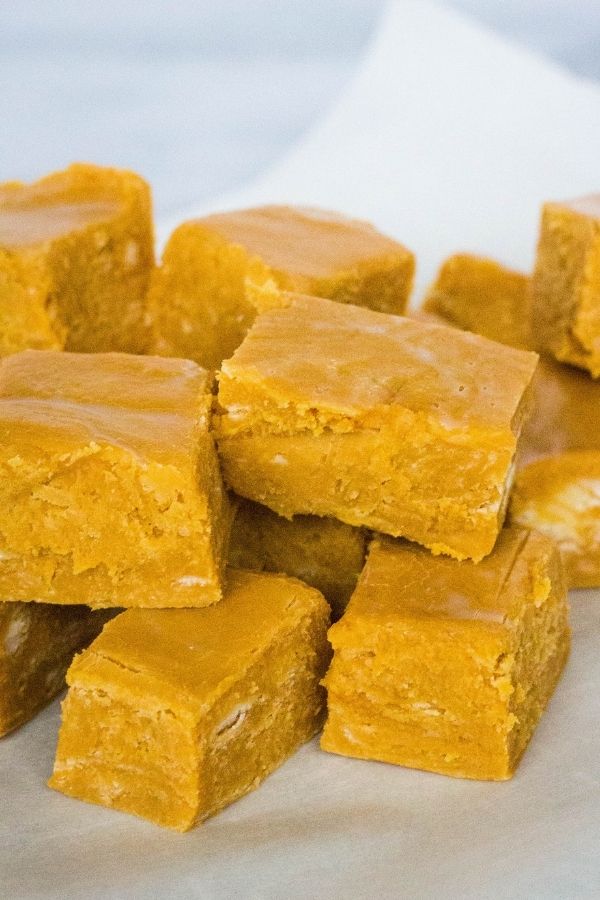 Squares of salted caramel fudge stacked on a piece of parchment paper
