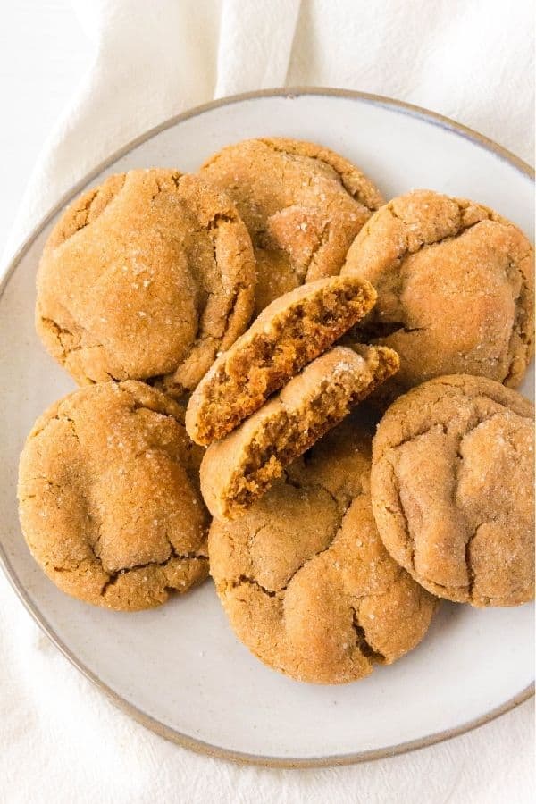 Seven molasses crinkle cookies on a cream-colored plate, with one cookie broken in half in the middle.