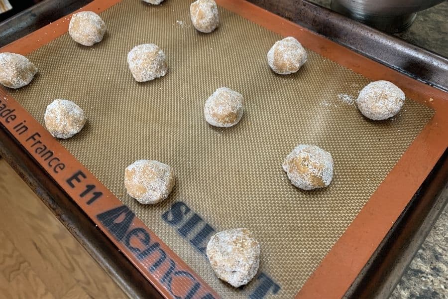 Twelve rolled balls of molasses cookie dough on a baking sheet, ready to be baked.