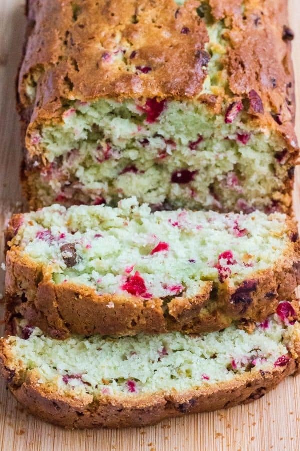 sliced loaf of homemade cranberry pistachio bread, with two slices laying flat, showing the moist interior of the bread.