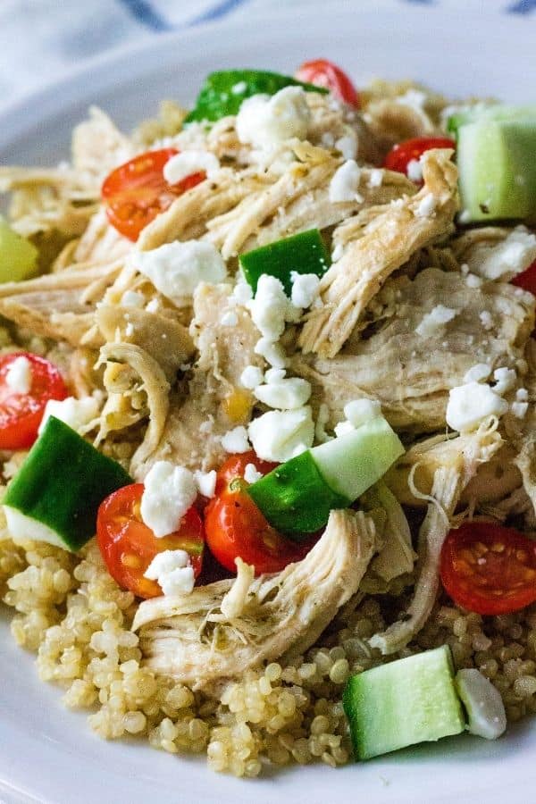 Quinoa, Greek chicken, cucumbers, tomatoes, and feta served on a white plate