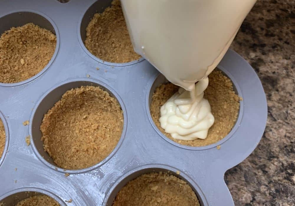 a piping bag squeezing cheesecake filling into the crusts