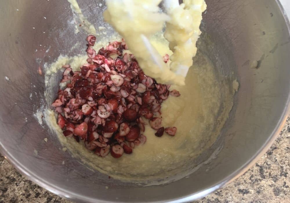 chopped cranberries added to butter mixture in a mixing bowl for making cranberry pistachio bread