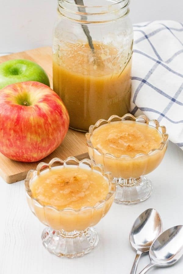 two glass bowls filled with Instant Pot applesauce, with apples and a jar of applesauce in the background.