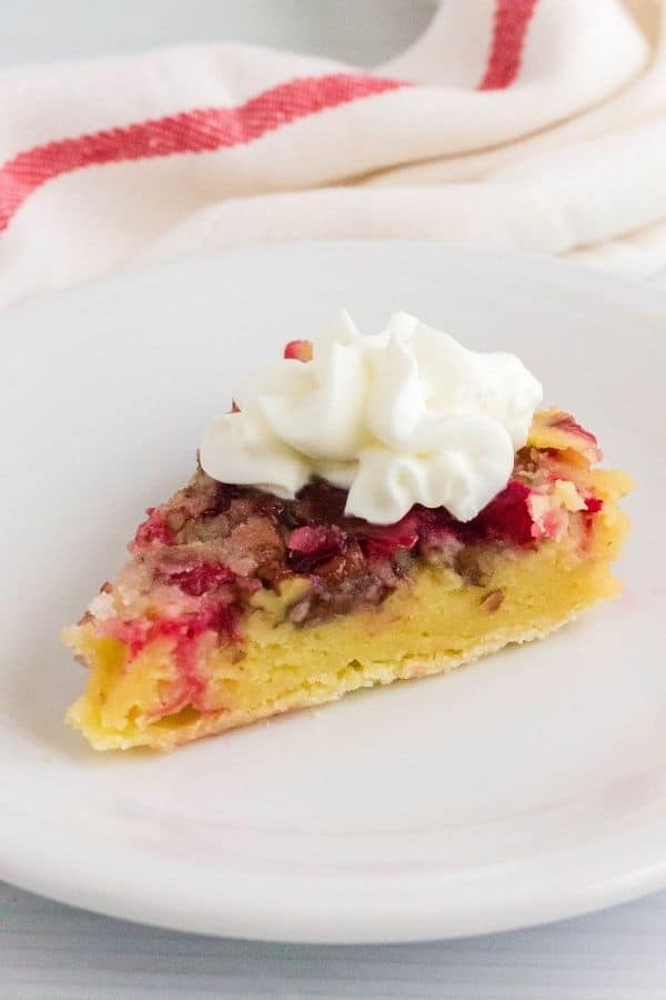 side view of a slice of Nantucket cranberry pie on a white plate, topped with whipped cream