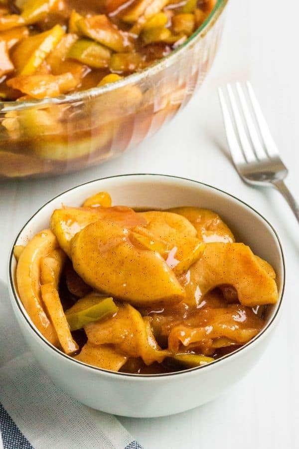 a cream-colored bowl filled with Instant Pot fried apples, with a serving bowl full of cinnamon apples in the background