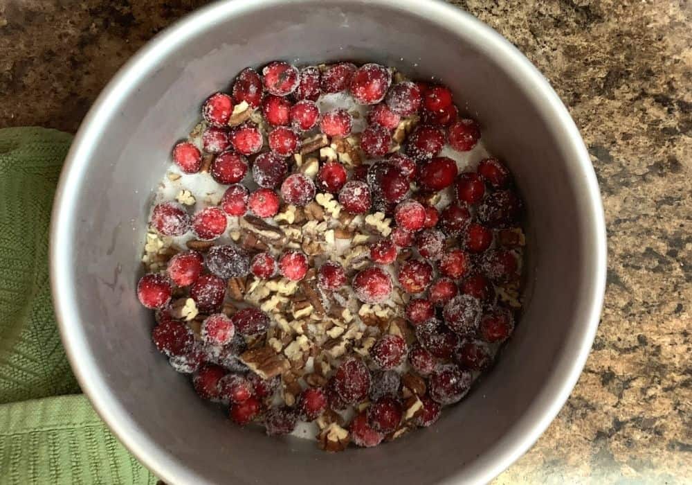 A pie pan with cranberries, pecans, and sugar in it for making cranberry pie.