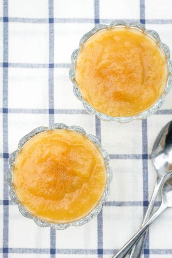 aerial view of two glass bowls of pressure cooker applesauce, topped with cinnamon, on a blue and white checked towel