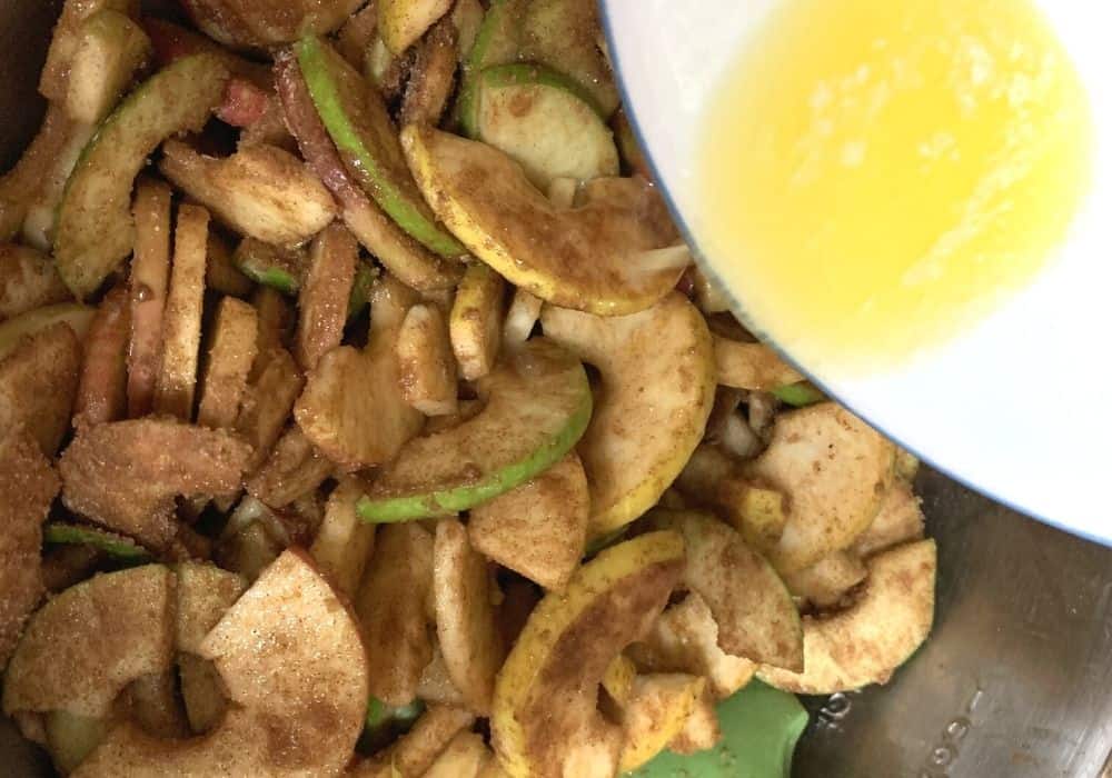 melted butter being poured over apples coated with cinnamon sugar mixture.