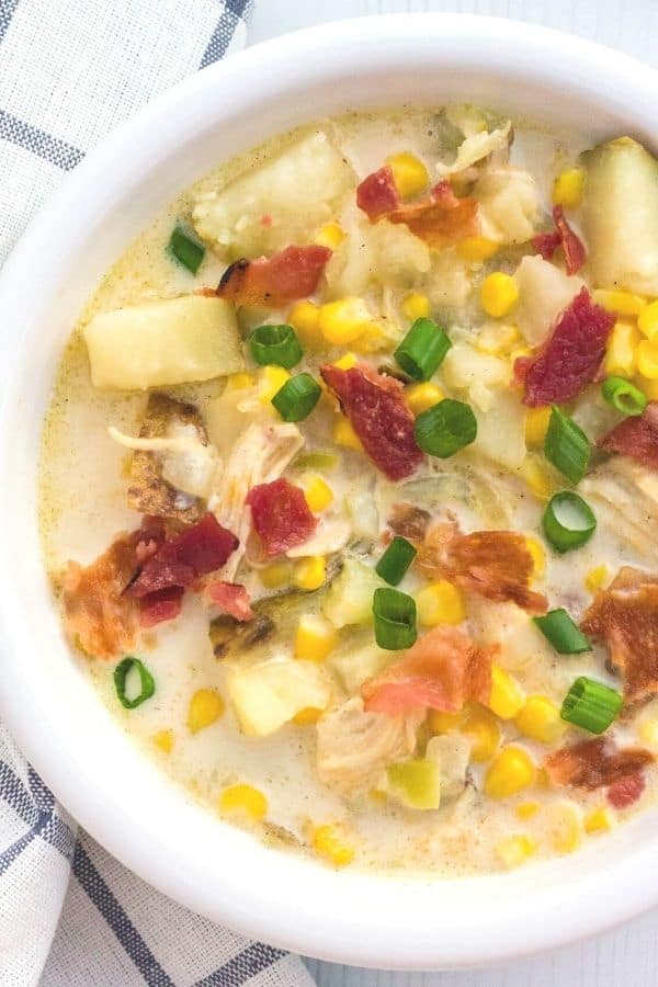 a white bowl filled with pressure cooker corn and chicken chowder, topped with sliced green onions and crumbled bacon