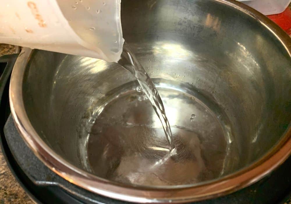 water being poured into the insert pot of the Instant Pot for steaming tamales