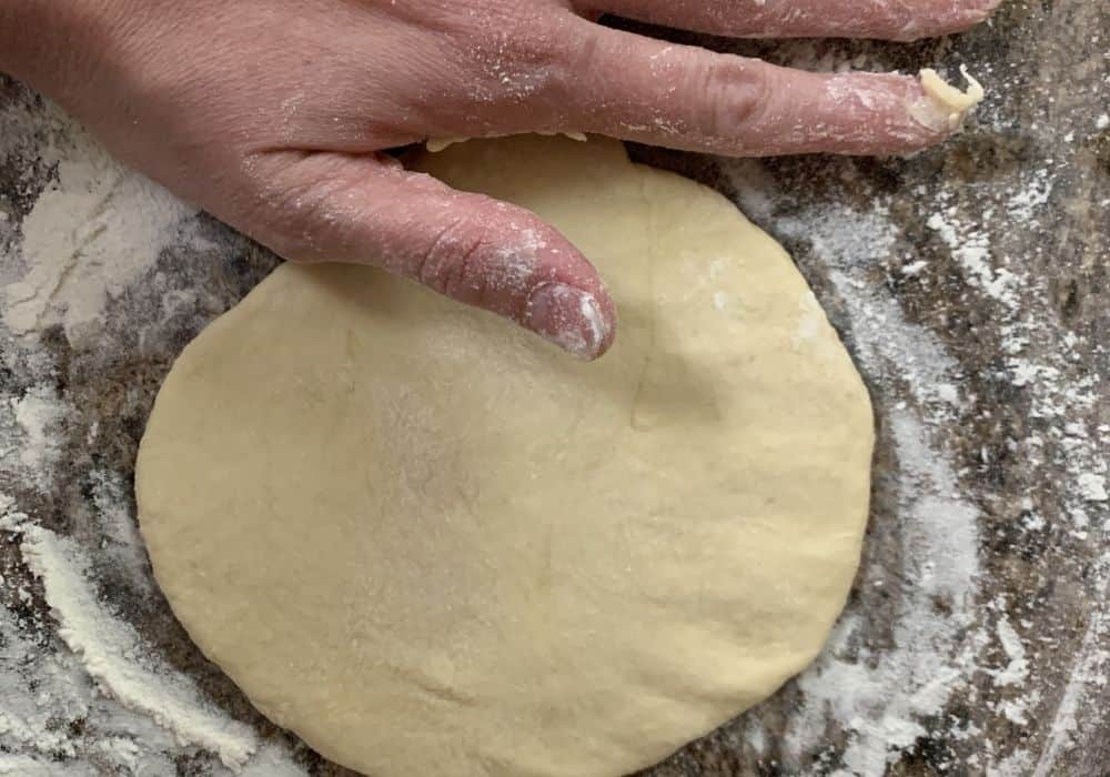 a round of naan dough rolled out on a floured surface
