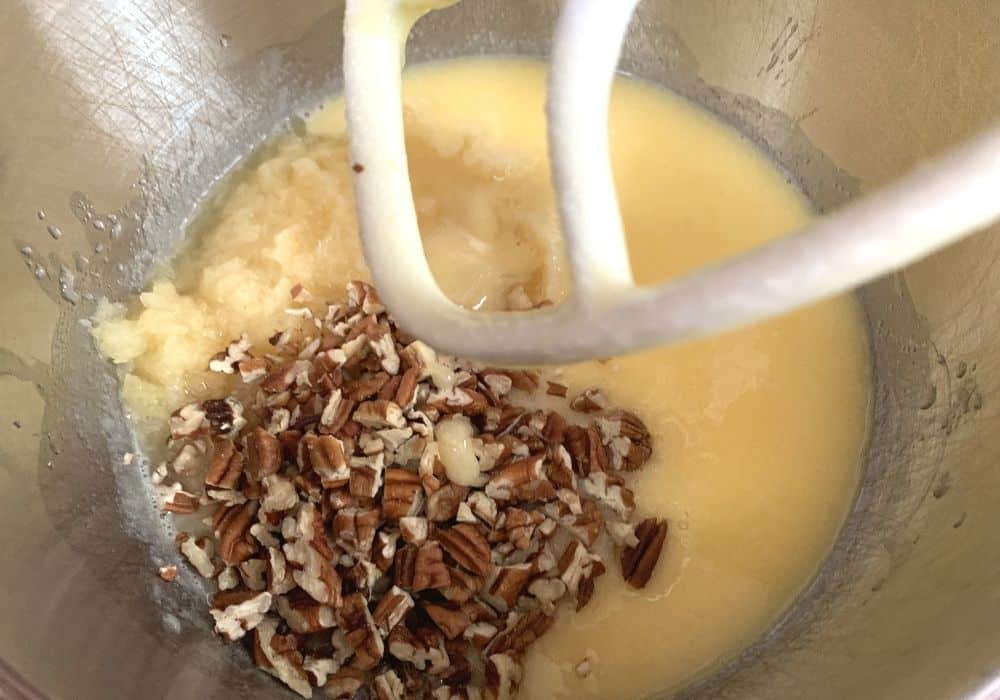 crushed pineapple and chopped pecans added to a mixture of oil, sugar, and eggs in the bowl of a stand mixer.