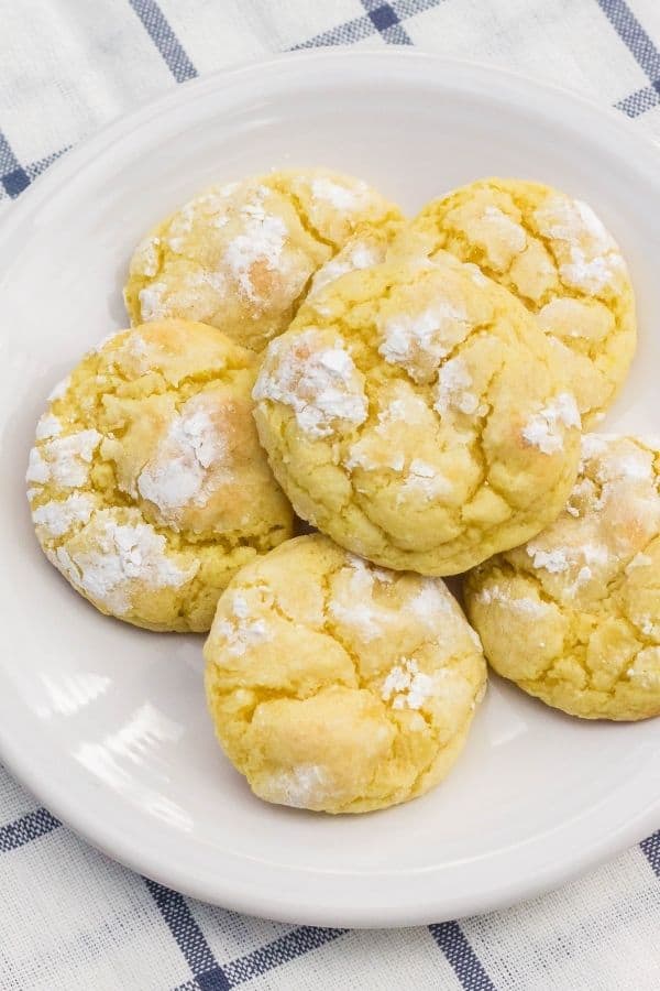Six lemon pudding crinkle cookies, topped with powdered sugar, on a white plate