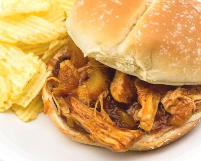 Instant Pot Hawaiian BBQ pulled chicken on a bun, on a white plate next to some potato chips