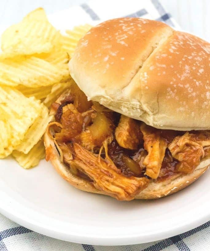 Instant Pot Hawaiian BBQ pulled chicken on a bun, on a white plate next to some potato chips